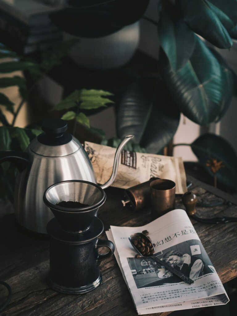 Black coffee grinder next to a stainless steel kettle on a table